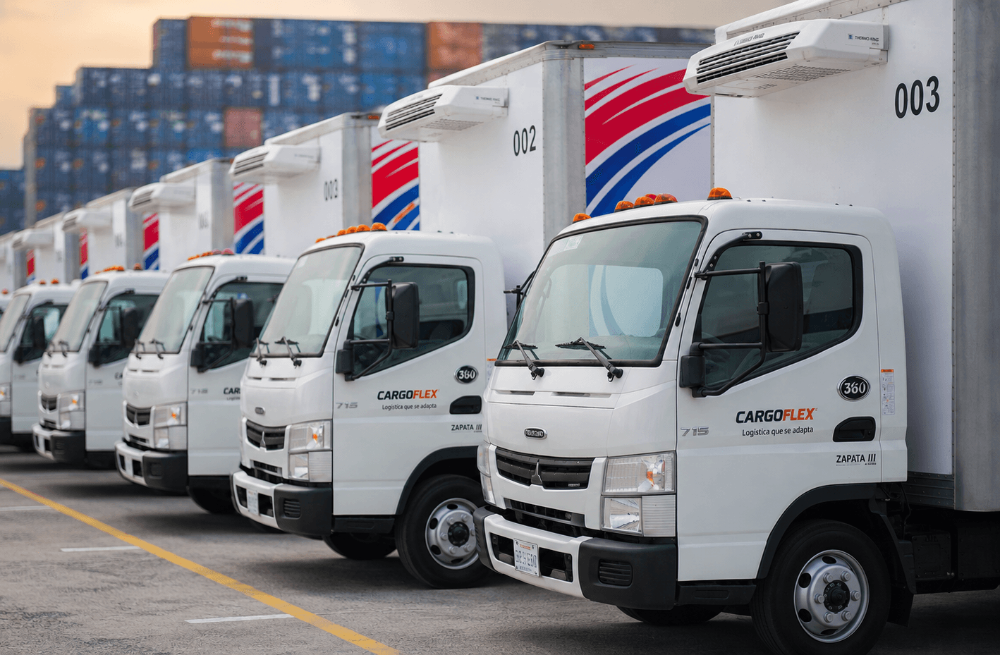 Flota de camiones de caja rotulados de CargoFlex formados frente a contenedores en Monterrey